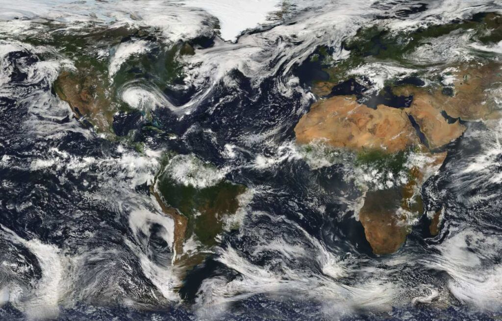 Satellite view of Earth showing North and South America on the left, Europe and Africa on the right, with swirling cloud formations across the Atlantic Ocean and visible landmasses, forests, deserts, and weather systems